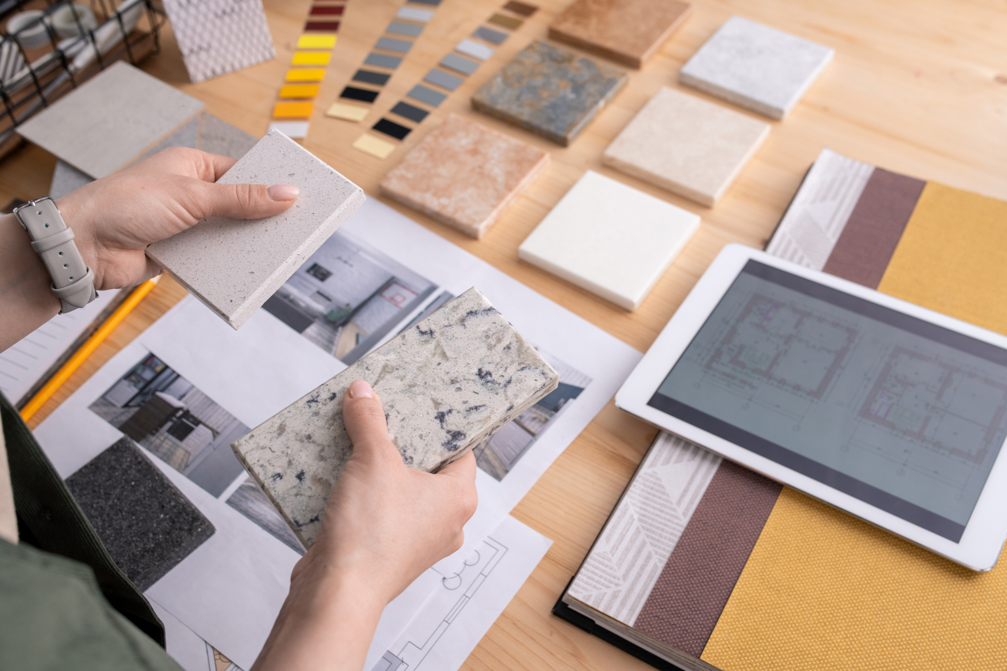 Hands of young female designer holding two samples of marble tile over table